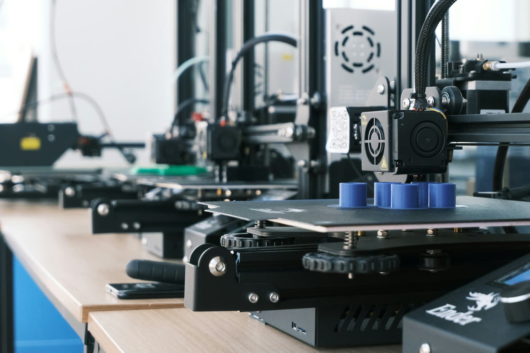 A row of desktop 3D printers running side by side on a workshop bench