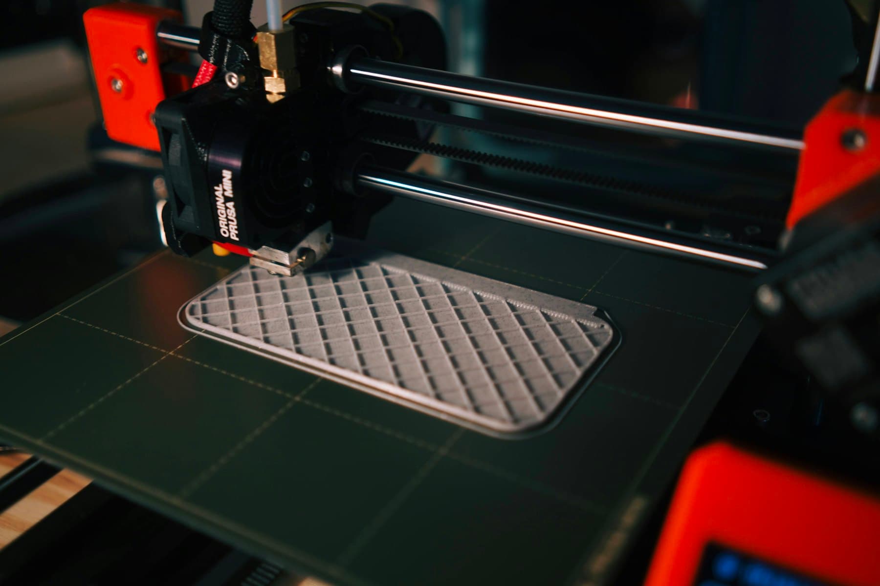 A flat part being built layer by layer on a print bed, its internal infill pattern still visible before the top surface closes over it